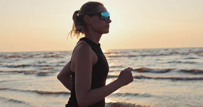 Woman running on beach at sunset in black sportswear. Healthy lifestyle and fitness. Cardio workout