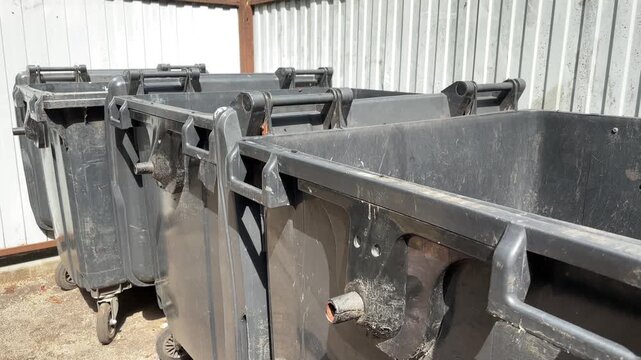 A row of black public municipal trash containers stands outdoors, urban sanitation, waste collection, city maintenance, environmental management.