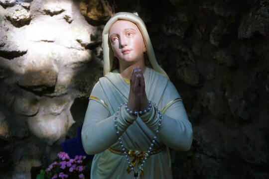 Statue von betender Heiliger Bernadette vor Fels in Grotte bei Sonne am Abend im Sommer