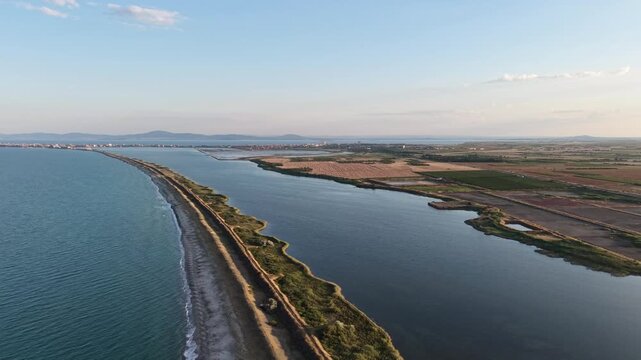 Aerial panoramic view of Pomorie salt pans and narrow sand spit road next to the sea at sunset