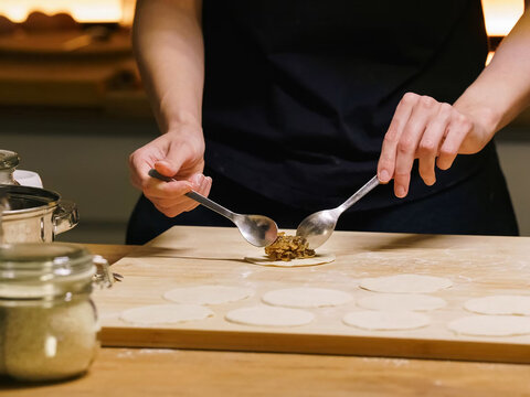 Hands filling dumplings with mushroom stuffing on wooden board, homemade cooking process