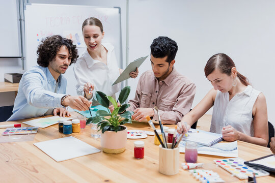 Diverse group of young people in painting class together in a bright studio classroom. Multicultural group of adults men and women engaged in a creative art project