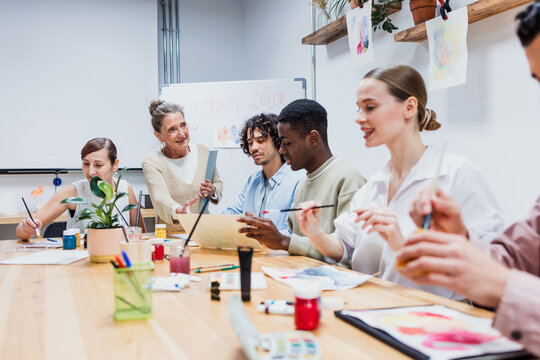 Diverse group of young people in painting class together in a bright studio classroom. Multicultural group of adults men and women engaged in a creative art project