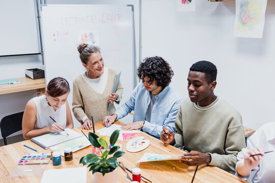 Diverse group of young people in painting class together in a bright studio classroom. Multicultural group of adults men and women engaged in a creative art project