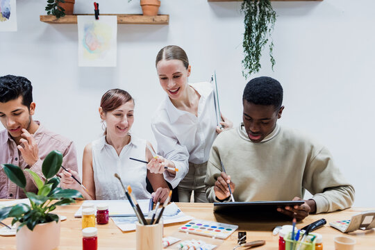 Diverse group of young people in painting class together in a bright studio classroom. Multicultural group of adults men and women engaged in a creative art project