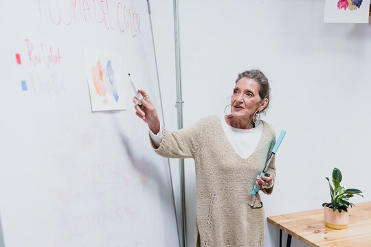 hispanic senior woman writing on whiteboard in classroom. elderly teacher in Education concept 
