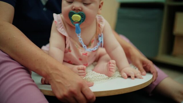 Baby sitting on a therapy disc, learning to balance, supported by an occupational therapist for developmental milestones