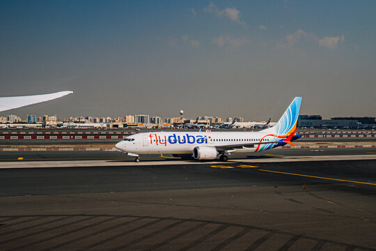 FlyDubai airplane taxiing on runway at Dubai International Airport with city skyline visible in the background