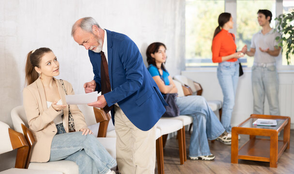 Queue of applicants in reception room, senior male manager talking to girl office-seeker. Job interview, labor policy, elimination of unemployment. Employer and applicant discuss employment contract