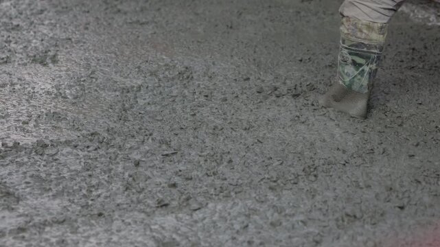 Leveling wet concrete surface with hand screed during floor construction