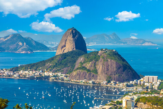 Stunning aerial view of Sugarloaf Mountain and Guanabara Bay in Rio de Janeiro, Brazil, featuring anchored boats and a vibrant blue sky on a sunny day.