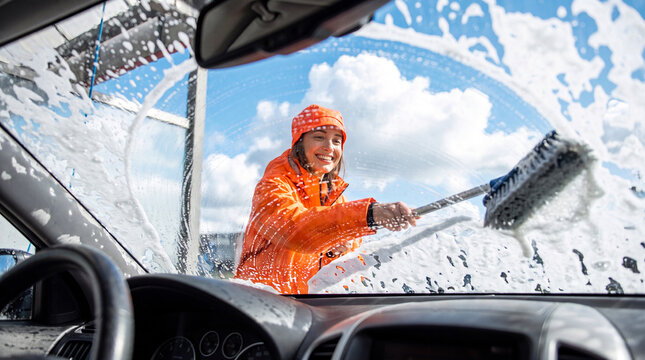 Woman washing car windshield with soap. Female driver cleaning vehicle glass with a squeegee brush.