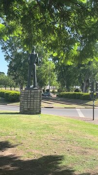 Urban square with a clock tower and a pedestrian viewpoint revealing a headless statue during a sunny day with cars driving along the busy streets of the city