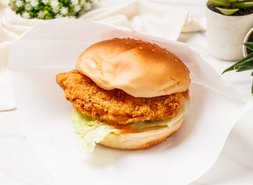 Crispy fried chicken burger in paper wrap. Delicious breaded chicken sandwich for fast food delivery.