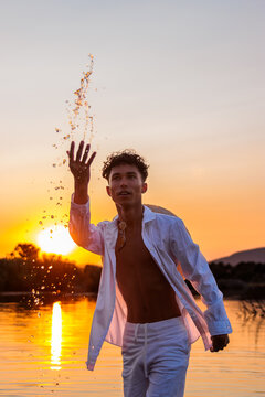 Young man playing with water splashes during summer sunset over a lake