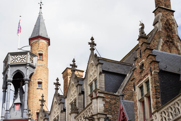 Fototapeta premium Historic architecture featuring intricate stonework and a tall clock tower with a flag, showcasing a blend of Gothic and Renaissance styles in a European cityscape