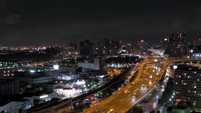 Night timelapse of illuminated expressway traffic and city skyline near Tokyo Bay, Japan. Fast-moving car lights and urban buildings under cloudy sky.