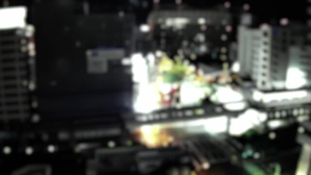 Abstract timelapse of defocused city lights and buildings at night in Naha, Okinawa, Japan. Soft bokeh urban background with glowing windows and street illumination.