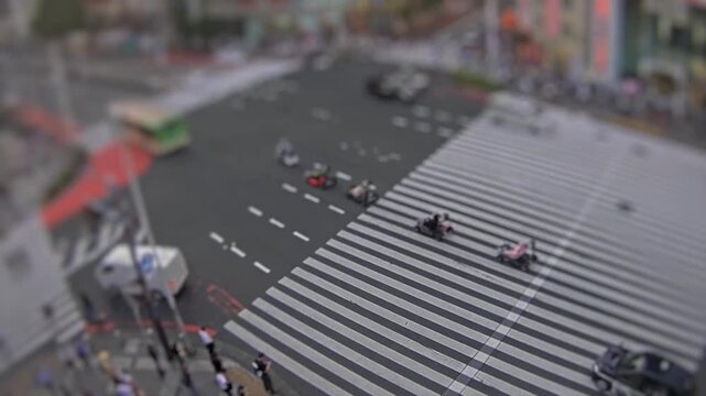 High-angle tilt-shift style timelapse of a large pedestrian crosswalk with traffic and commuters moving through a city intersection in Tokyo, Japan.