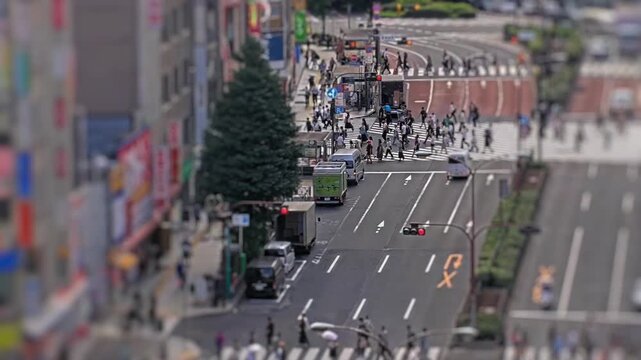 Tilt shift style timelapse of a busy Tokyo intersection with cars buses and pedestrians moving through crosswalks in daylight.