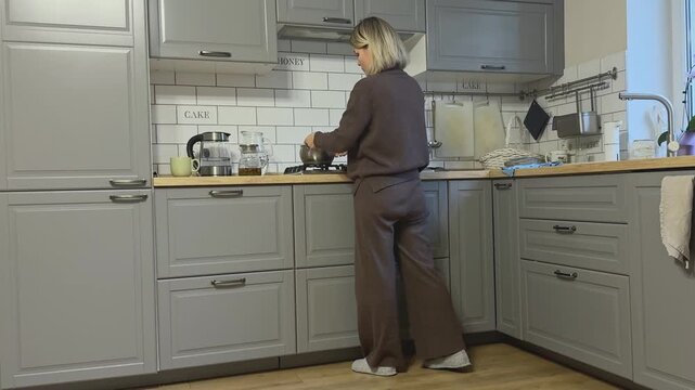 Female opens lower drawer, takes pot and puts it on gas stove ready to cook.