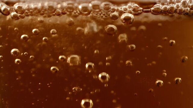 A close-up shot of a carbonated brown beverage with many small bubbles rising to the surface, creating a fizzy texture.
