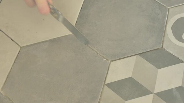 Hand Cleaning Tile Grout Lines from Adhesive with Putty Knife During Tile Installation