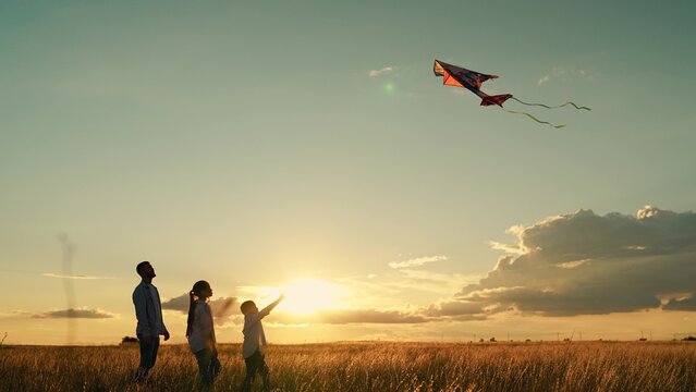 Happy family with child playing with kite in meadow. Dad children play on grass, child dreams flying. Family picnic, father, son daughter playing with kite outdoors. People travel together, nature sky