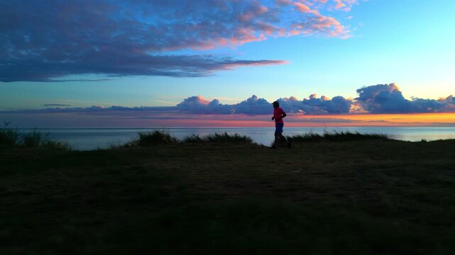A senior adult jogs along the lakeside path at sunrise, the sky painted in hues of pink and orange. The peaceful scene represents a healthy lifestyle and the joy of morning exercise.