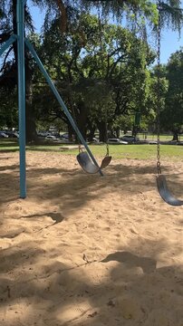 Lone empty swing moving back and forth in a deserted sandy playground on a summer paceful day