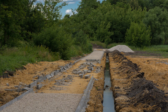 crushed stone, sand and curbstone next to a ditch with water
