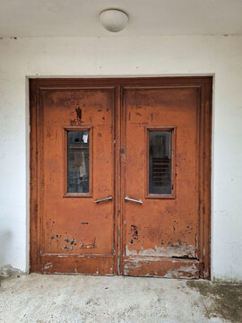 Weathered orange double door with small windows in abandoned hospital wall