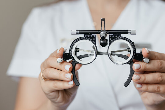 Close-up of ophthalmologist holding trial frame for visual acuity testing in an eye care clinic. Professional optometry equipment used for vision diagnostics and prescription lenses.