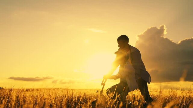 Dad helps child son ride bike. Dad teaches child wearing safety helmet to ride bicycle Family in meadow. Child rides bicycle. Kid dad play together, sunset. Child boy dream learns to ride bicycle, sun