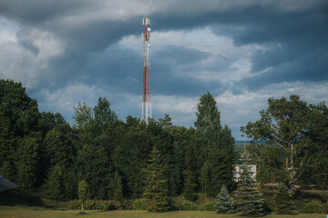 Obraz premium Communication tower standing tall amidst lush green trees under a cloudy sky, showcasing a blend of technology and nature in a rural landscape