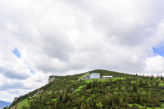 A panoramic view of Rax Mountain in Austria showcases a striking contrast between lush greenery and a dramatic cloudy sky with hints of soft blue, capturing the essence of nature whe