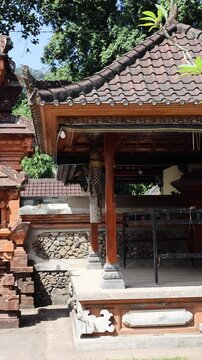 Ornate Balinese temple gate with carved terracotta details and adjacent pavilion in bright daylight, showing symmetrical entrance, stone textures, and tropical setting