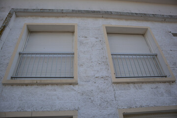Fototapeta premium Two closed windows with roller shutters and safety railings on weathered facade