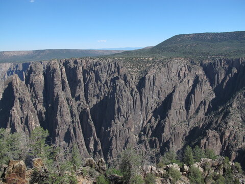 Dramatic sheer canyon walls and rugged rock spires under a clear blue sky in a remote high desert landscape of the American West.
