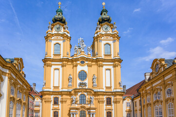 Obraz premium Melk Abbey in Austria features stunning baroque architecture with intricate details in warm yellow hues under a clear blue sky, with twin towers rising majestically above the central facade adorned