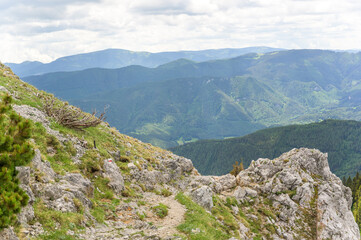 Fototapeta premium A breathtaking view of Rax Mountain in Austria reveals lush green valleys and rugged rock formations beneath a partly cloudy sky where the vibrant greens of the hills contrast with the grey rocks