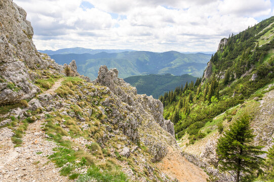 A breathtaking view of the Rax Mountains in Austria showcasing rugged rocky terrain lush green valleys and a vibrant blue sky dotted with clouds and sunlight casting a warm glow on the land