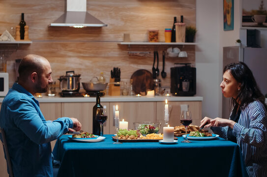 Happy couple eats and drinks wine during a festive dinner in the kitchen, enjoying candlelight, conversation and romantic time together.
