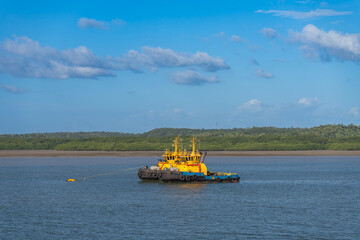 Fototapeta premium Two bright yellow and blue tugboats moored together on a tranquil blue river, pulling a secure line. The background features a dense green coastal forest under a beautiful partly cloudy sky
