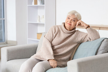 Fototapeta premium Beautiful thoughtful senior woman sitting on sofa at home