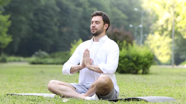 Handsome man practicing yoga on mat in park