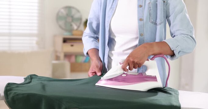 Woman ironing long sleeve shirt on board at home, closeup