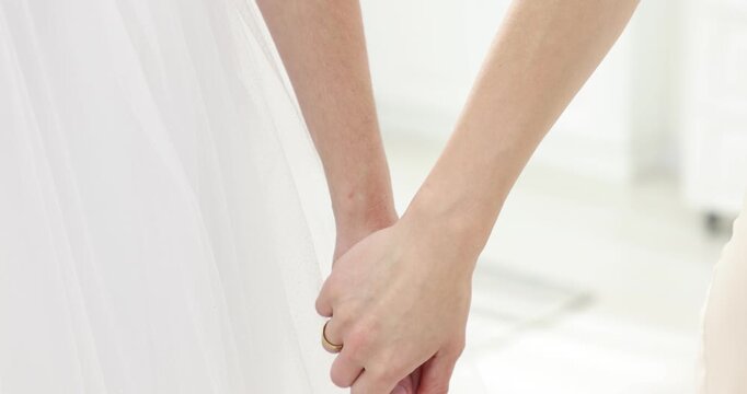 Lesbian wedding. Woman and her wife holding hands indoors, closeup. Camera moving down
