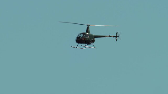 Helicopter flying horizontally across a bright blue sky, rotors spinning while providing aerial transportation in Antibes, France