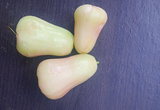 top view of three fresh green-white wax apples on a dark textured background